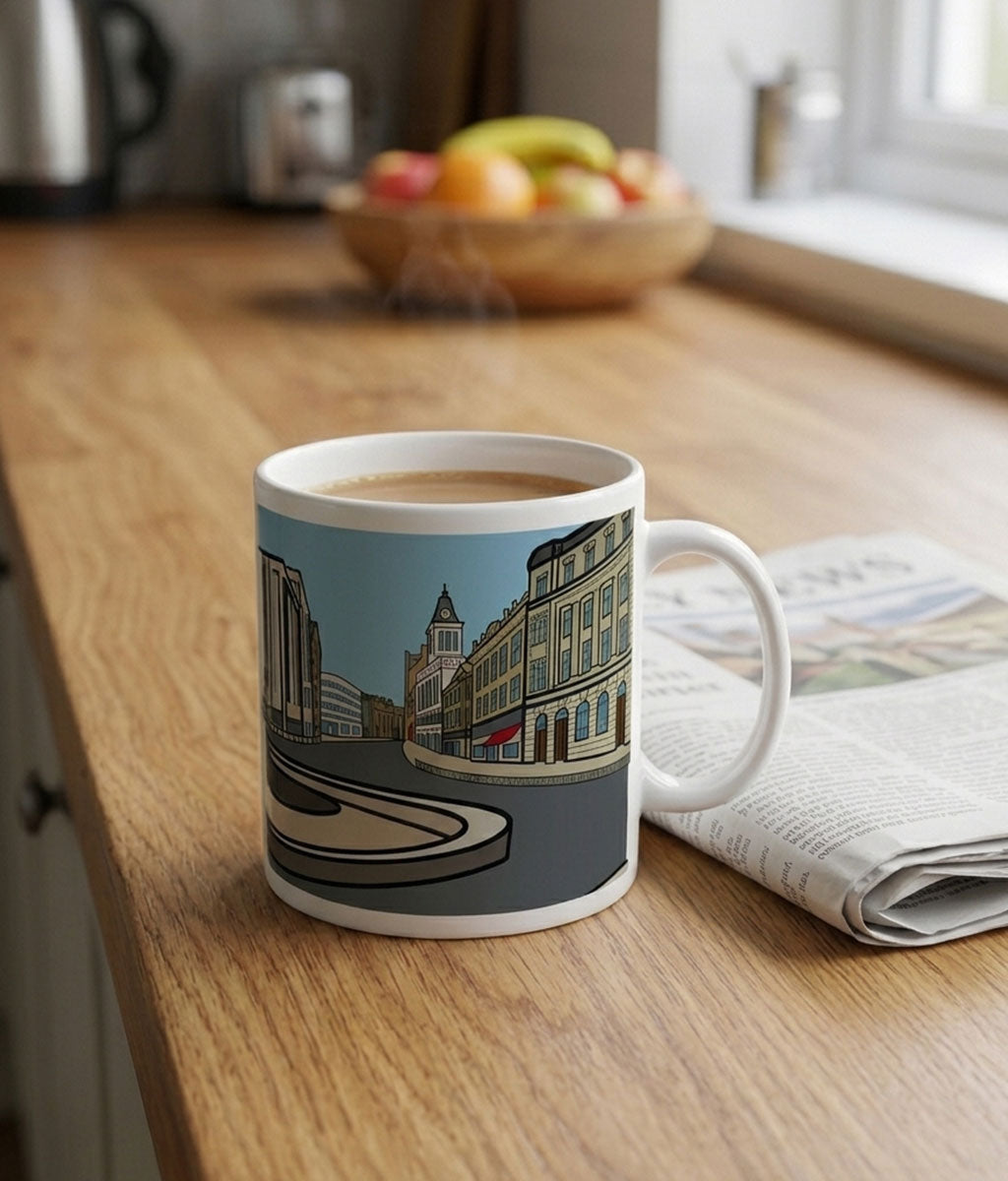 Mug with a cityscape design on a wooden table with a newspaper and fruit bowl in the background