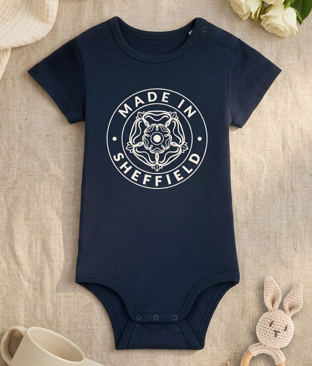Navy blue baby onesie with 'Made in Sheffield' print on a textured surface.