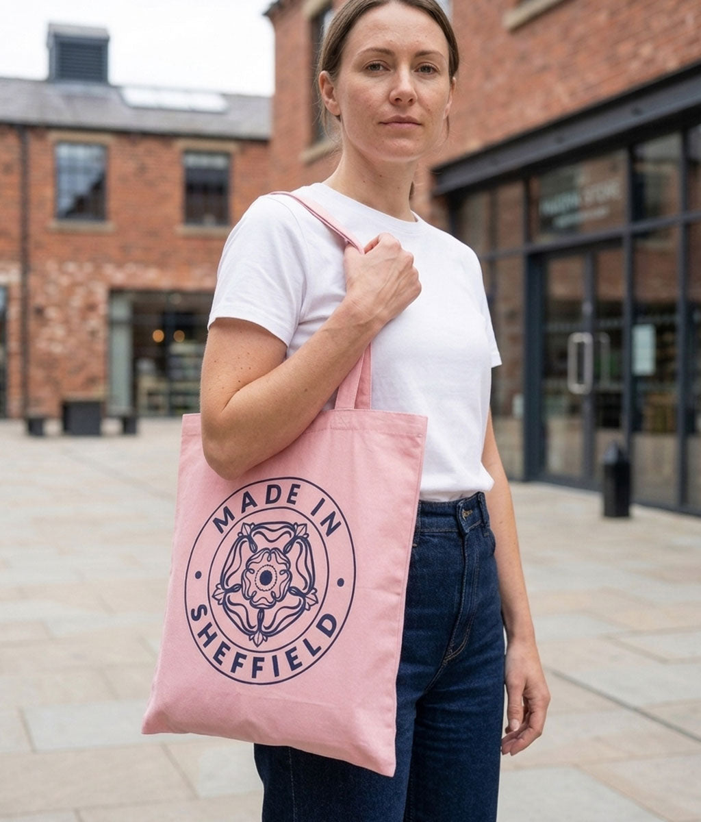Woman holding a pink tote bag with 'Made in Sheffield' design outdoors.
