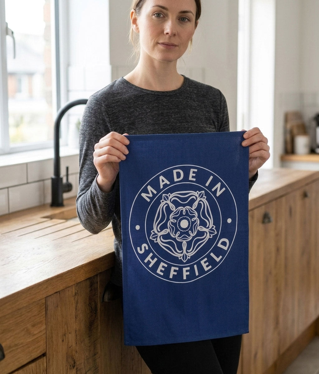 Person holding a blue towel with 'Made in Sheffield' text in a kitchen.