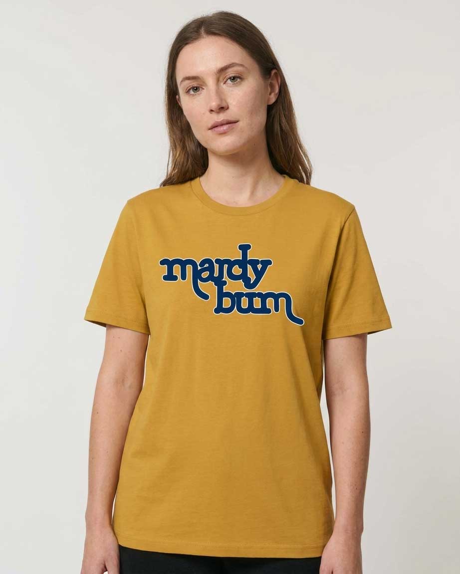 A woman wearing a mustard yellow t-shirt with the text 'mardy bum' printed in dark blue across the chest, set against a plain light gray background.