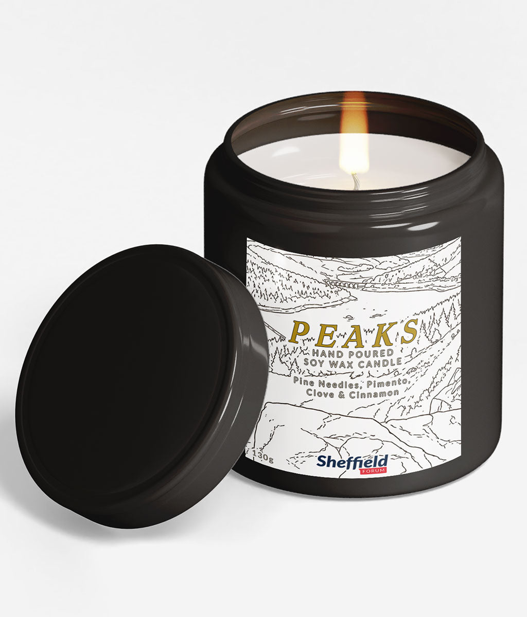 Black candle in a tin with 'PEAKS' label on a white background