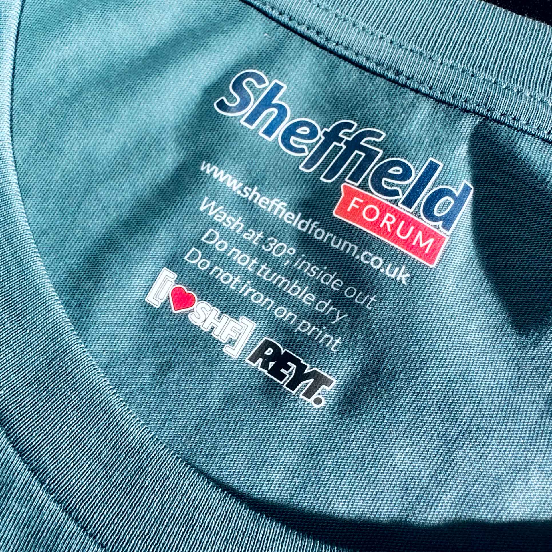 Close-up of a blue garment with 'Sheffield Forum' neck label branding and care instructions.