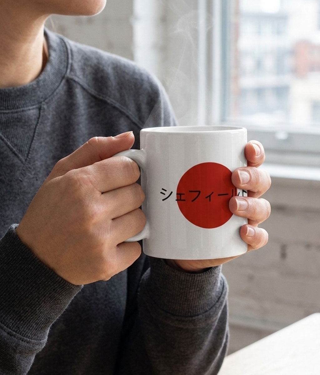 Person holding a white mug with a red circle and Japanese text, blurred background